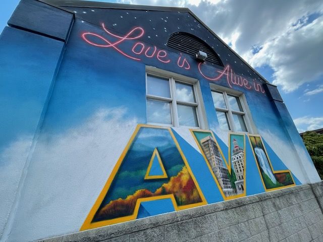 Mural on wall that says "Love is alive in AVL (Asheville)"