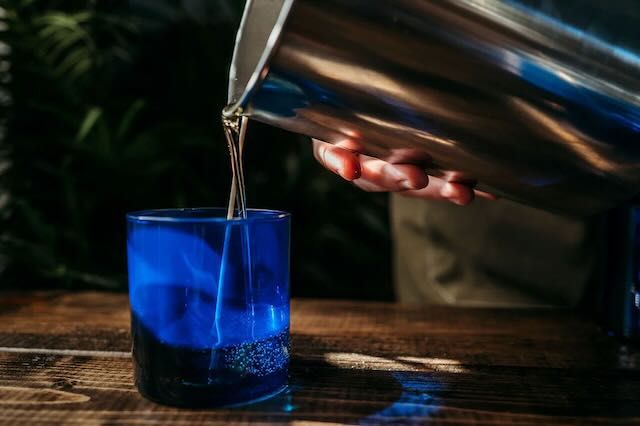 Silver vase pouring liquid wax into blue candle holder