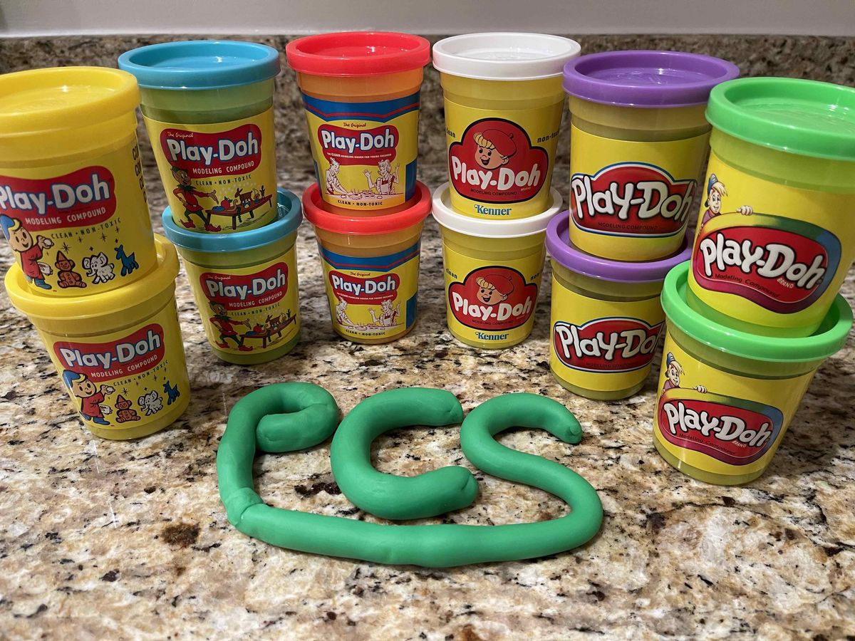 Play-Doh containers arranged behind "PCS" spelled out in green dough