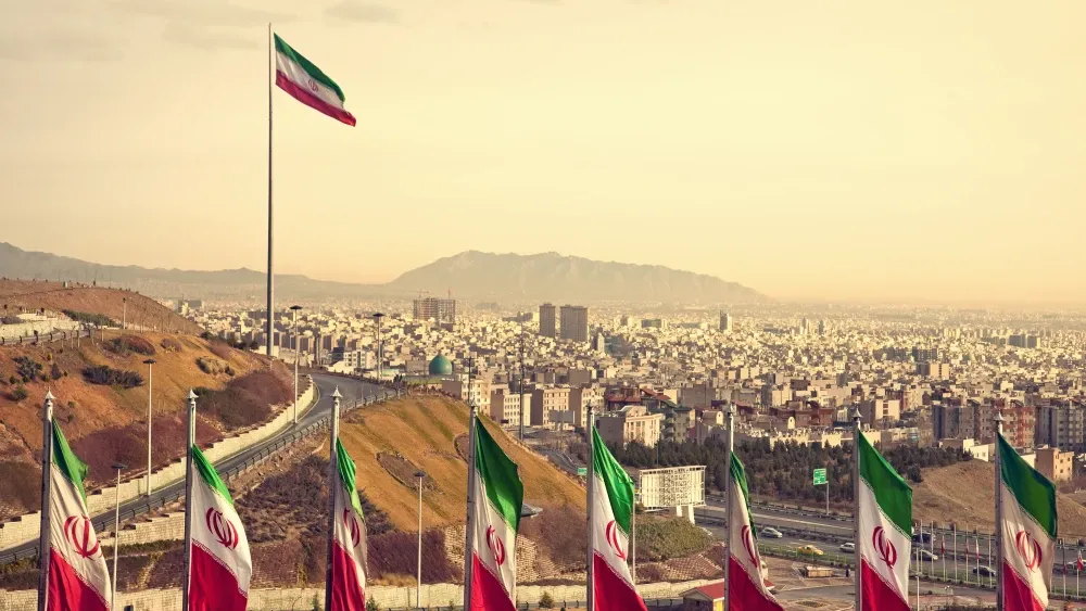 A smoggy view of Tehran unfolds behind a row of Islamic Republic flags.  Shutterstock
