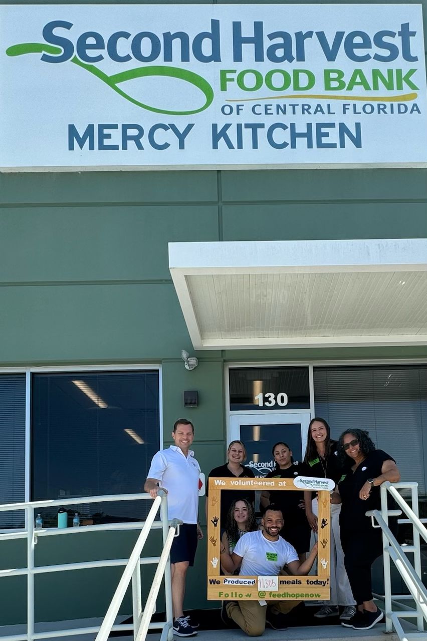 seven people posing for a selfie under the "Second Harvest Food Bank of Central Florida - Mercy Kitchen" sign