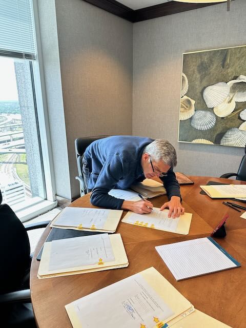 Man bent over table signing legal documents