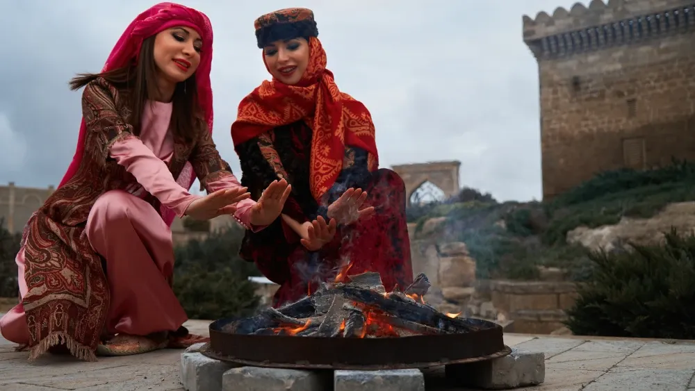 Azeri women in traditional Azerbaijani dress warm their hands above a springtime bonfire. Shutterstock
