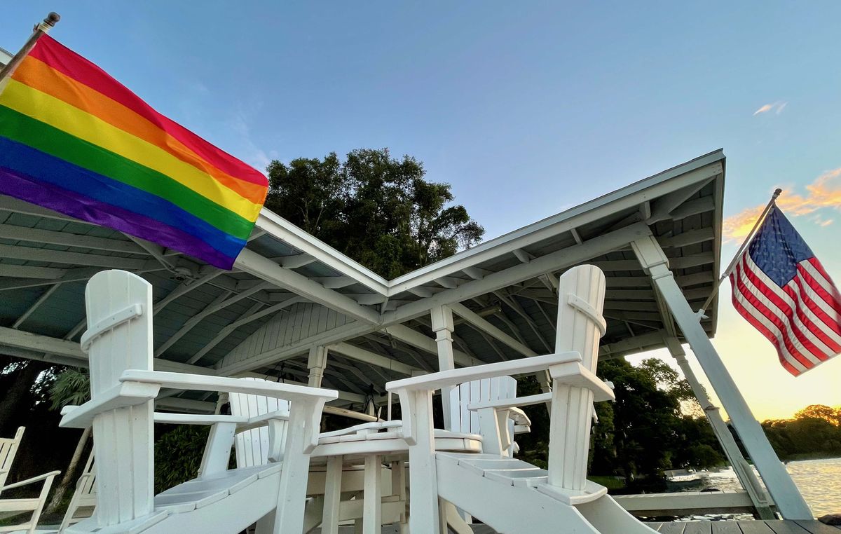 Pride flag (left) and American Flag (right) flying on a boat dock on a lake at sunset