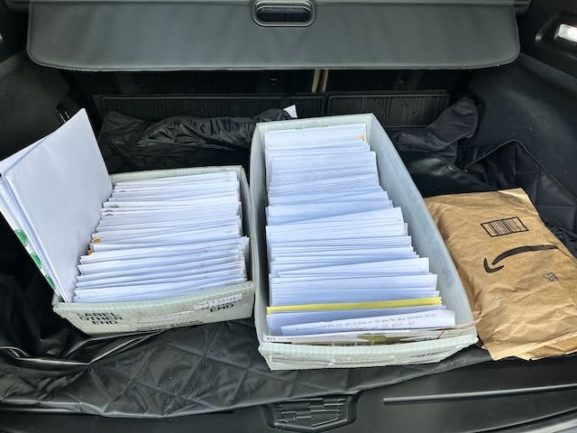 Two trays of mail in envelopes in the back trunk of a car