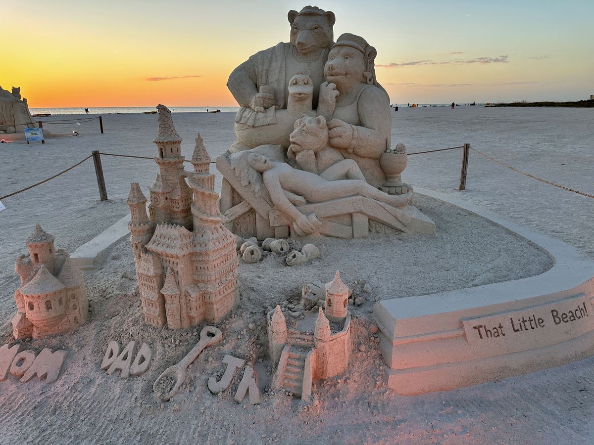 Sand castle art of three bears standing over a sleeping Goldilocks as they look at their damaged sand castles they'd built. Goldilocks damaged them after drinking too much and walking over them.