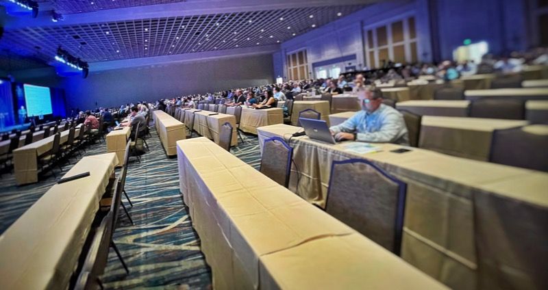 Large ballroom full of tables and chairs with people sitting and working