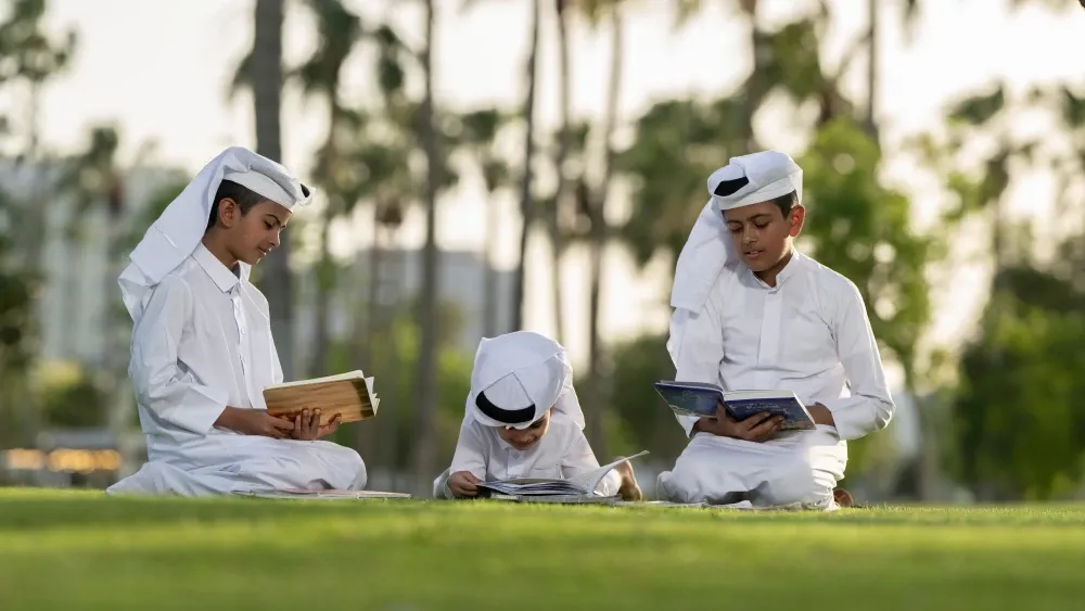 Young boys read on a lawn in Doha, Qatar, in May 2024.  Shutterstock