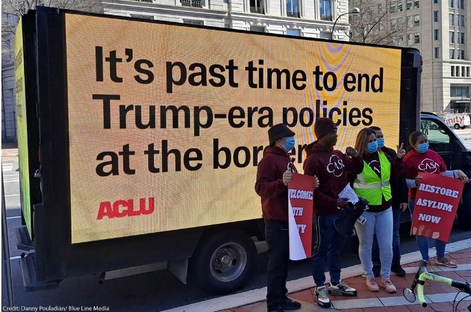 Picture of people in front of a digital signage truck that reads "It's past time to end Trump-era policies at the border" with the ACLU logo in the corner