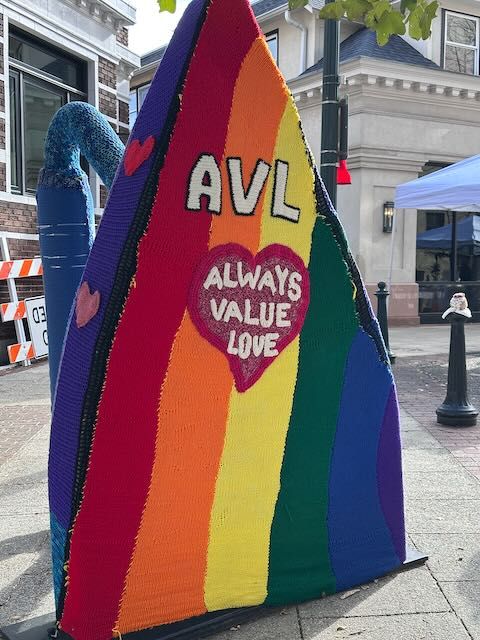 A large iron with a knitted rainbow-colored cover with "AVL and 'always value love'" in a heart