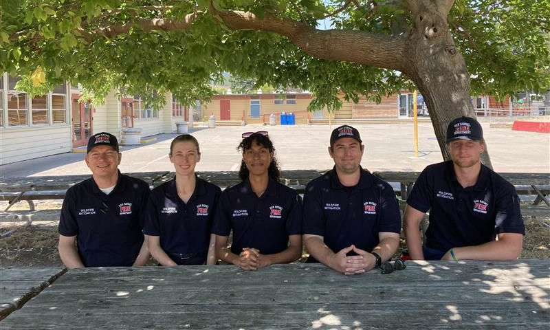 five smiling people under a tree wearing blue polos with the fire department logo