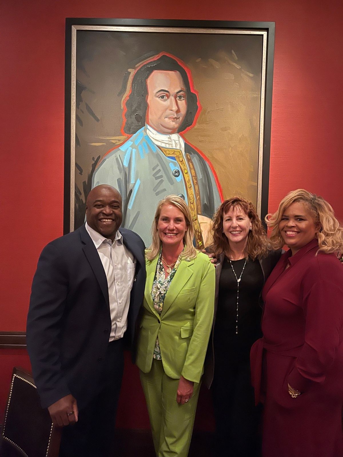 Group of one man and 3 women in front of portrait of George Mason