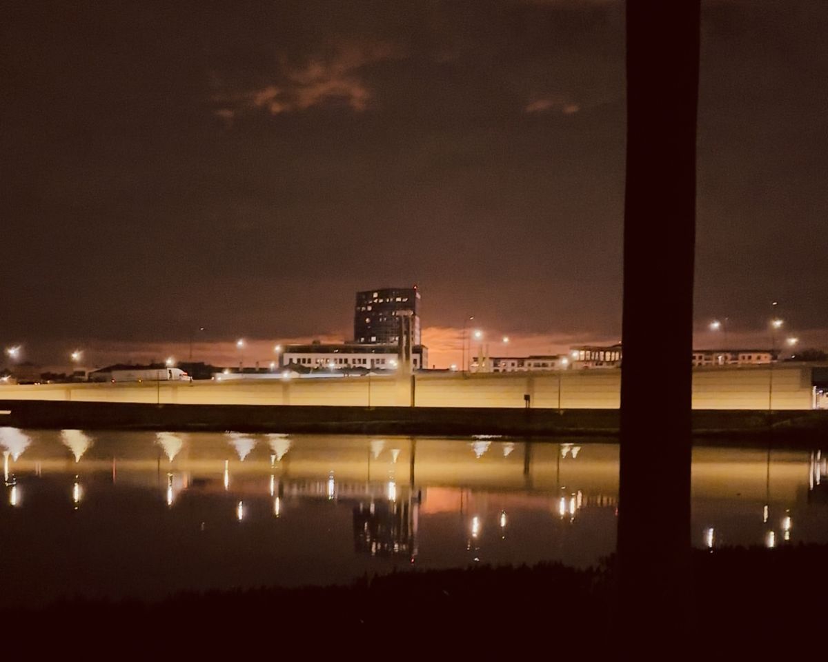 Night scene of orange glowing sky across a bridge and behind a building